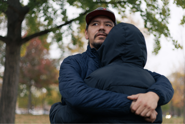 A man embraces another person. They are standing outside wearing coats.